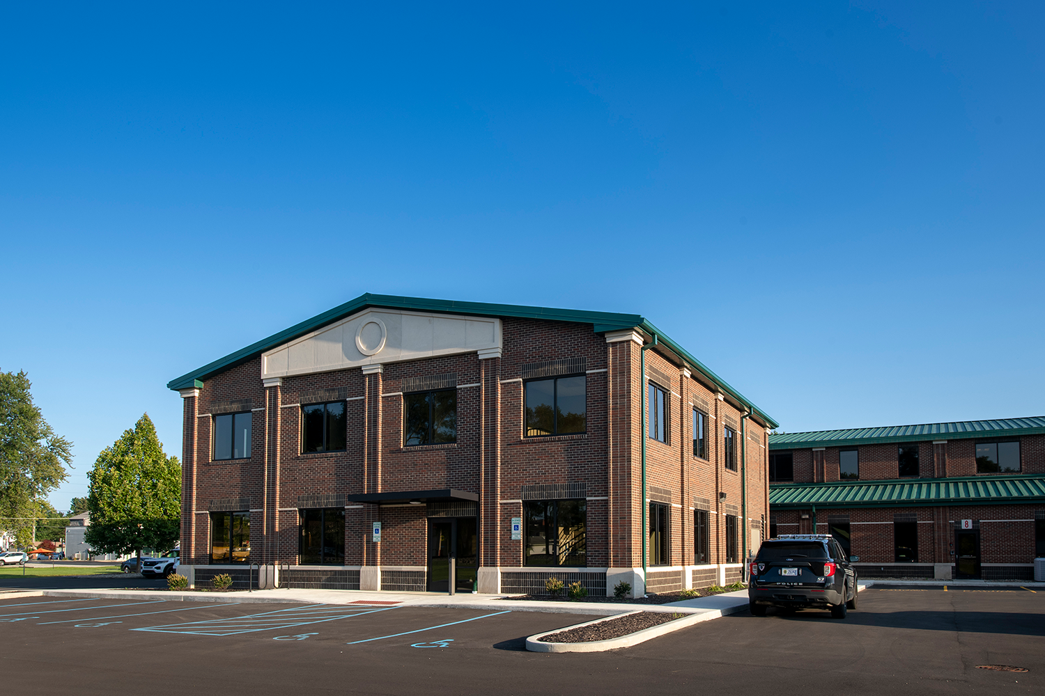 Front facade of New Haven City Hall and Police Station, with accessible parking and a green roof, under a clear blue sky. A police vehicle is parked out in front of the building.